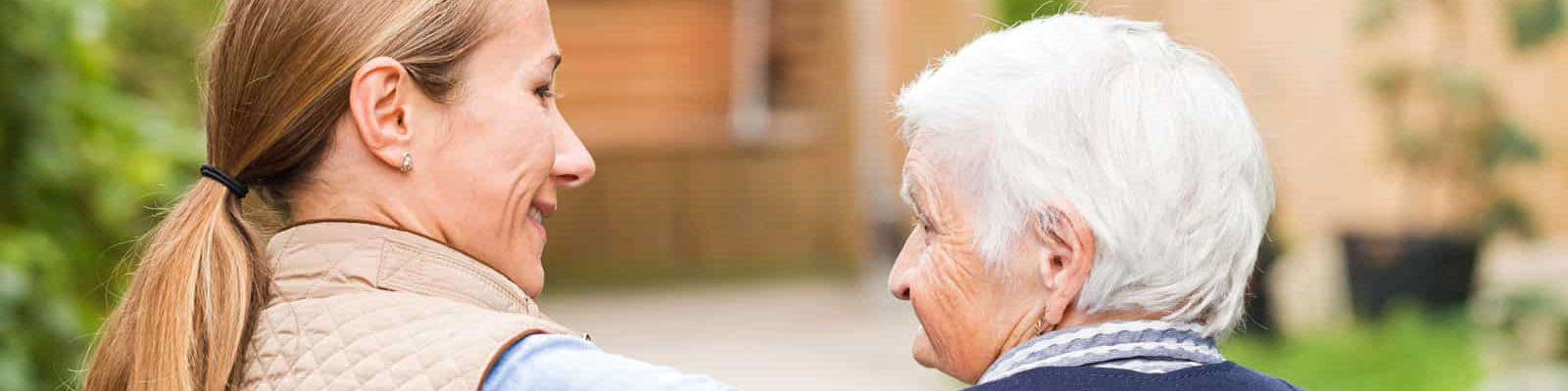 A senior woman walking outdoors beside her female nursing assistant