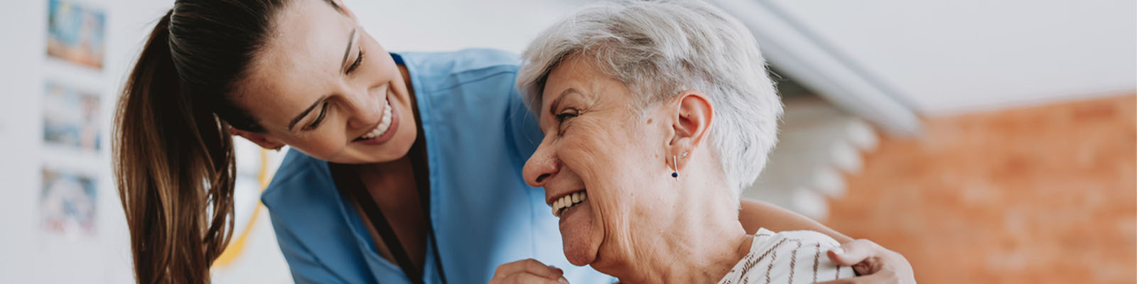 A senior woman sitting down looking up at her female nursing assistant